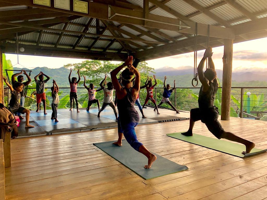 Group yoga class on open-air mountain platform at sunset